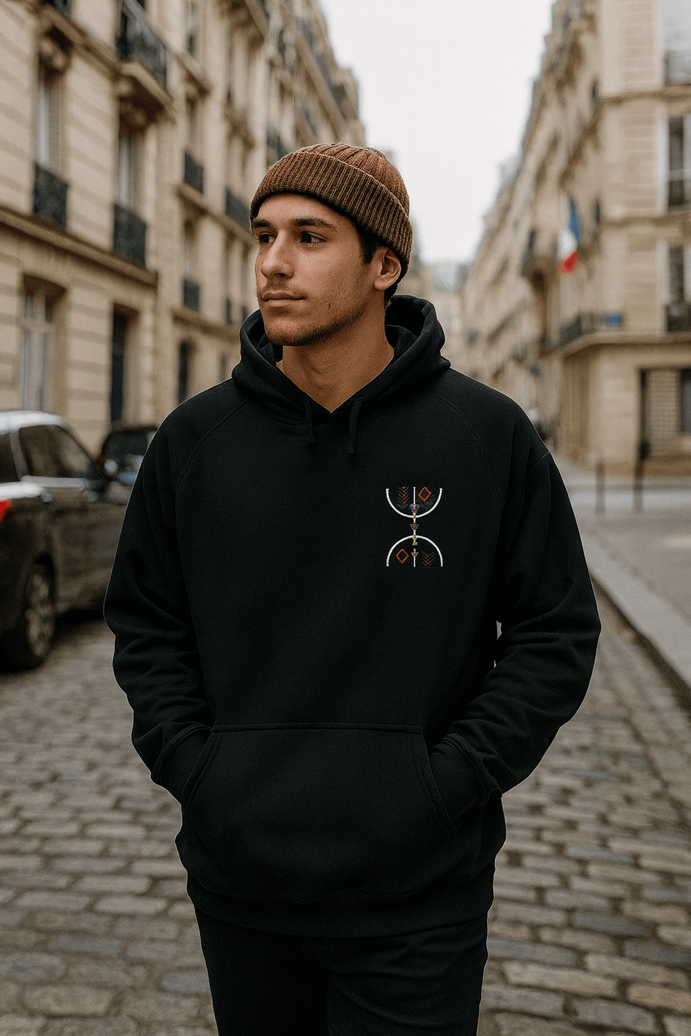 Schwarzer Hoodie mit bunter Stickerei, getragen von einem jungen Mann auf Kopfsteinpflasterstraße in der Stadt